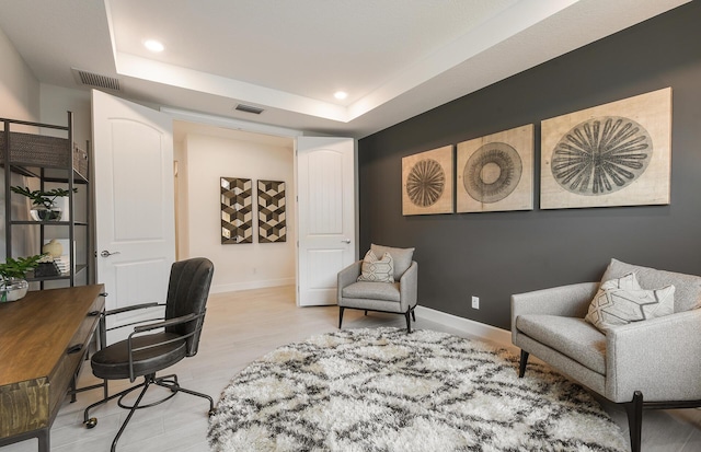 home office featuring a tray ceiling and light wood-type flooring