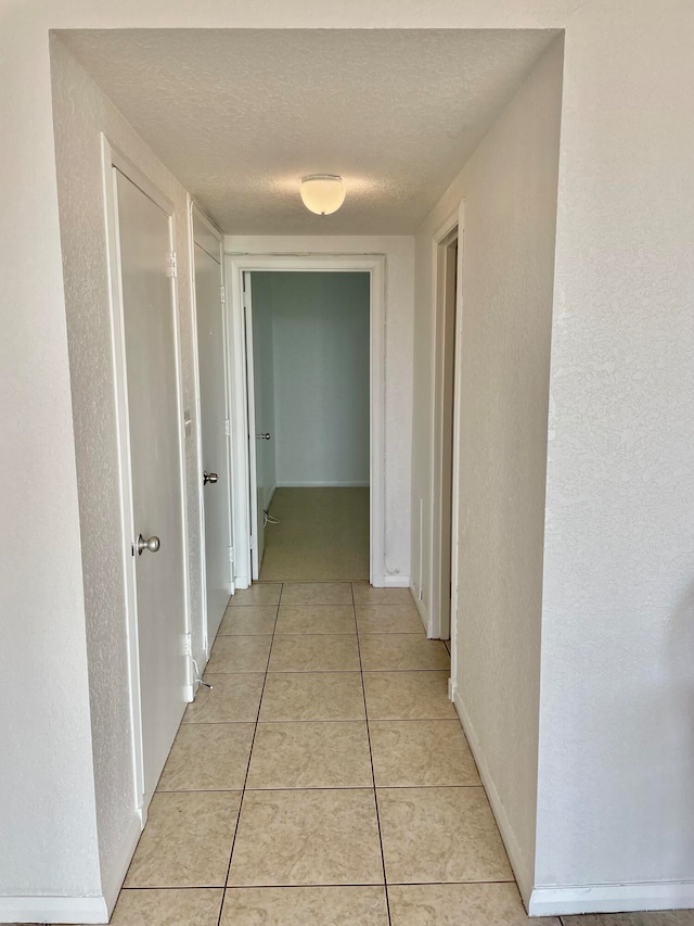 corridor featuring a textured ceiling and light tile patterned floors