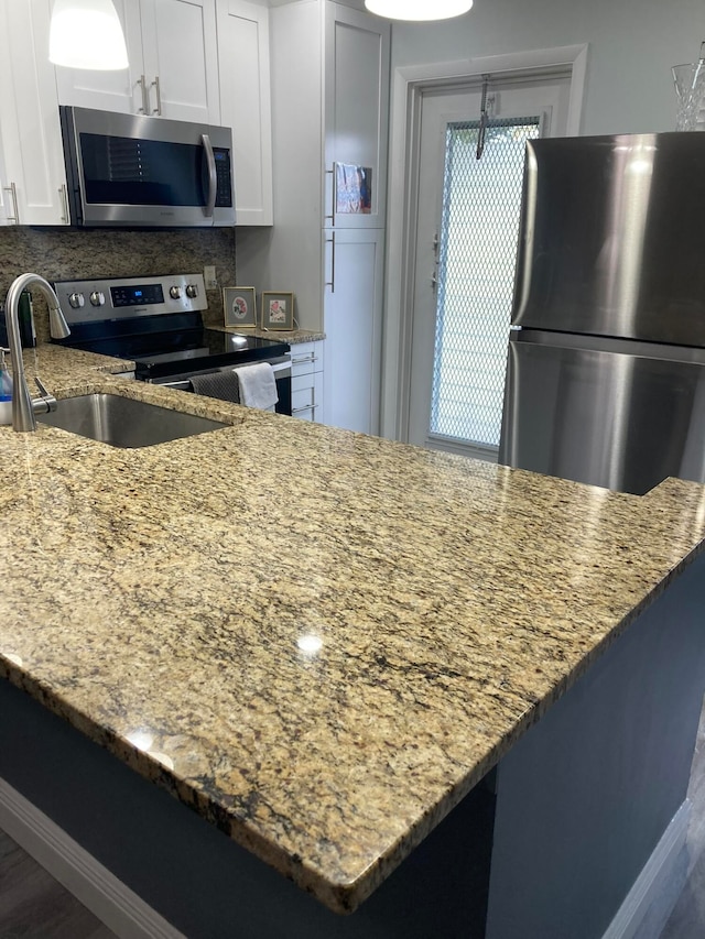 kitchen with stainless steel appliances, sink, light stone counters, tasteful backsplash, and white cabinets