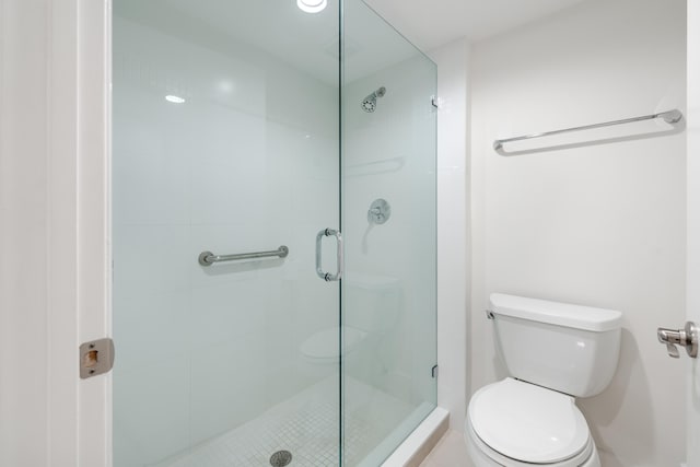 bathroom featuring a shower with door and toilet