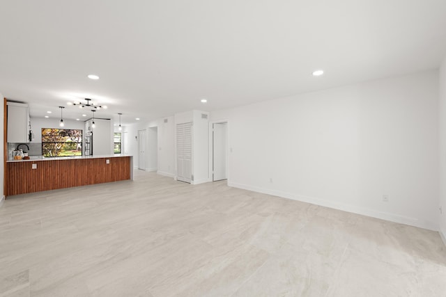 unfurnished living room featuring recessed lighting, baseboards, and a sink