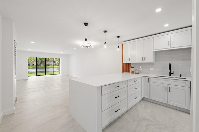 kitchen with decorative light fixtures, tasteful backsplash, kitchen peninsula, sink, and white cabinets