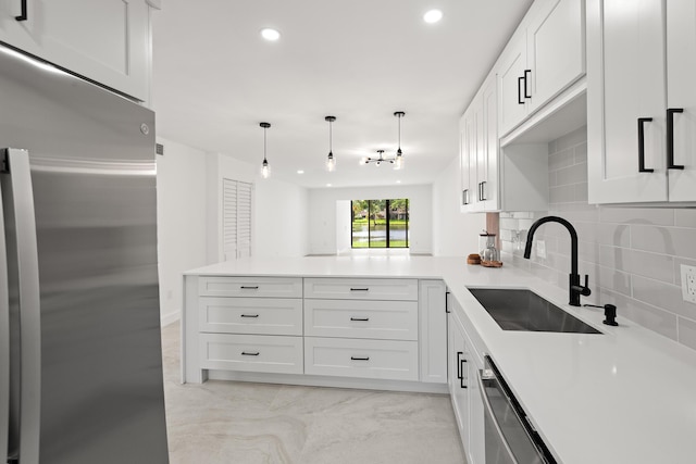 kitchen featuring backsplash, white cabinetry, a peninsula, stainless steel appliances, and a sink