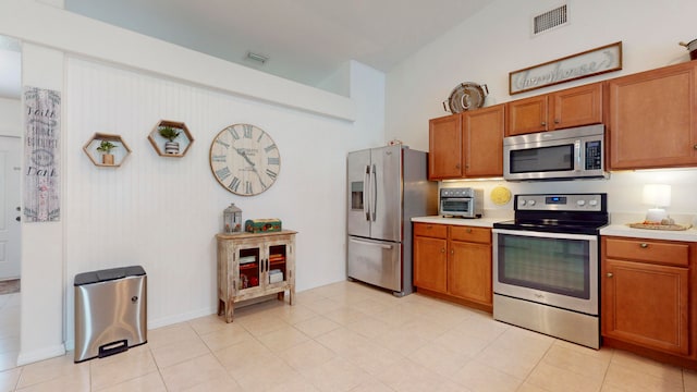 kitchen featuring appliances with stainless steel finishes, light tile patterned flooring, and vaulted ceiling