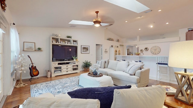 living room featuring light wood-type flooring, ceiling fan, and lofted ceiling with skylight