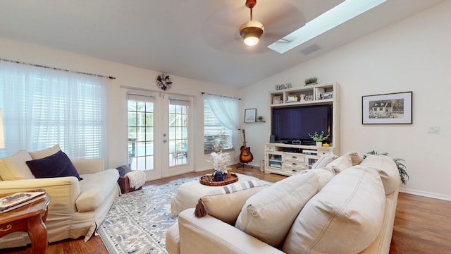 living room with hardwood / wood-style floors, ceiling fan, vaulted ceiling with skylight, and french doors