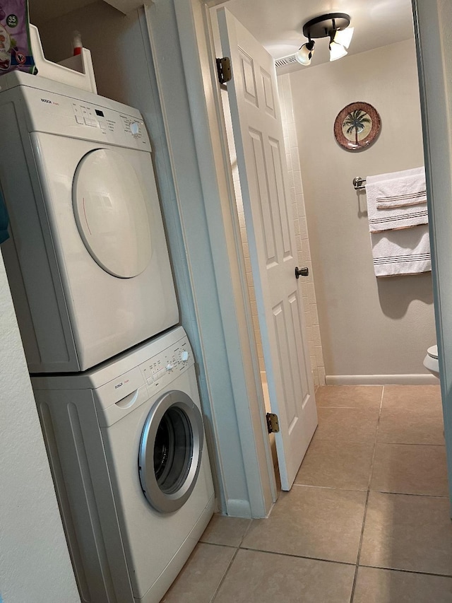 laundry room with light tile patterned floors, baseboards, stacked washer and clothes dryer, and laundry area