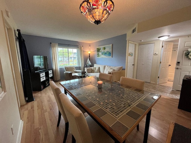 dining space featuring light wood-type flooring, visible vents, and a textured ceiling