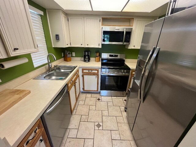 kitchen featuring white cabinets, a sink, stone tile flooring, light countertops, and appliances with stainless steel finishes