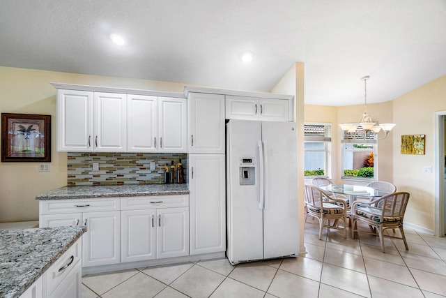 kitchen with white refrigerator with ice dispenser, decorative backsplash, a chandelier, white cabinetry, and light stone counters