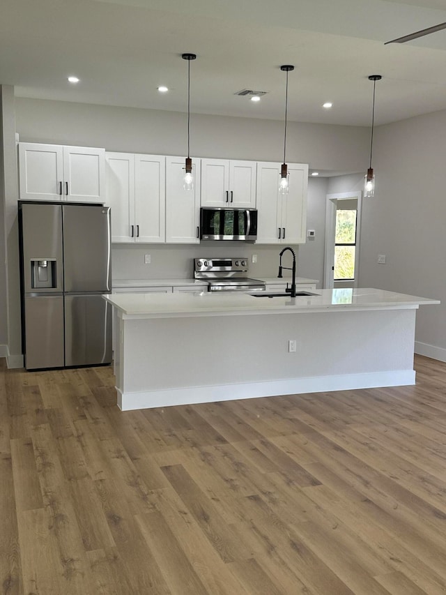 kitchen featuring white cabinetry, sink, decorative light fixtures, a kitchen island with sink, and appliances with stainless steel finishes