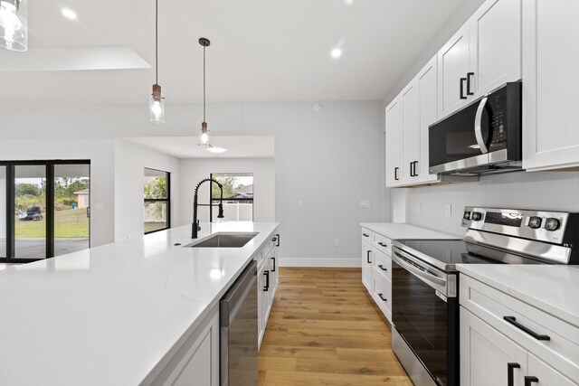 kitchen with sink, hanging light fixtures, light wood-type flooring, white cabinetry, and stainless steel appliances