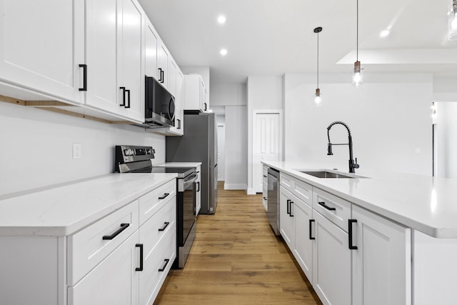 kitchen with stainless steel appliances, a sink, white cabinetry, hanging light fixtures, and a center island with sink