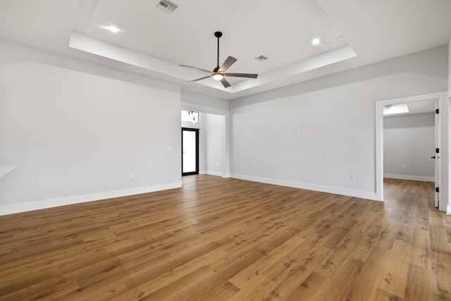 unfurnished room with baseboards, visible vents, a raised ceiling, ceiling fan, and light wood-type flooring