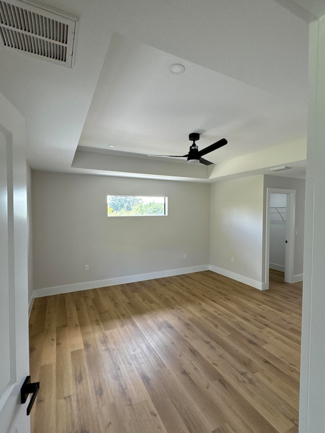 unfurnished room featuring a raised ceiling, light hardwood / wood-style flooring, and ceiling fan