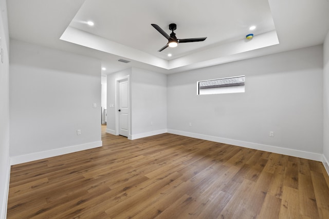 unfurnished room with wood finished floors, a raised ceiling, visible vents, and baseboards