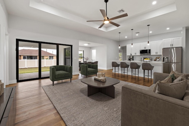 living area featuring light wood finished floors, a raised ceiling, visible vents, and baseboards