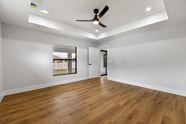 spare room with baseboards, a raised ceiling, a ceiling fan, wood finished floors, and recessed lighting