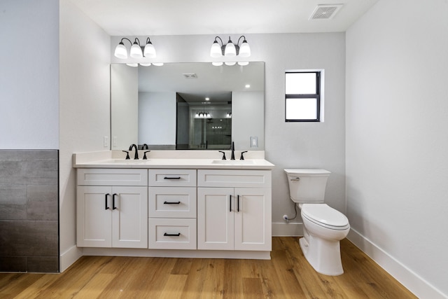 bathroom featuring wood finished floors, visible vents, a sink, and double vanity