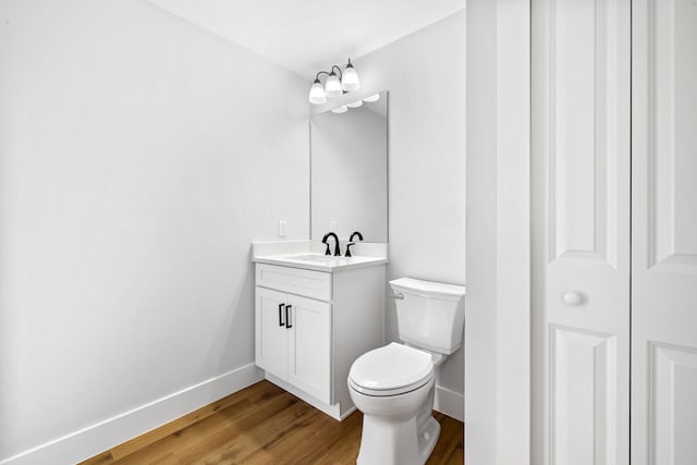 bathroom with toilet, wood finished floors, vanity, baseboards, and a closet