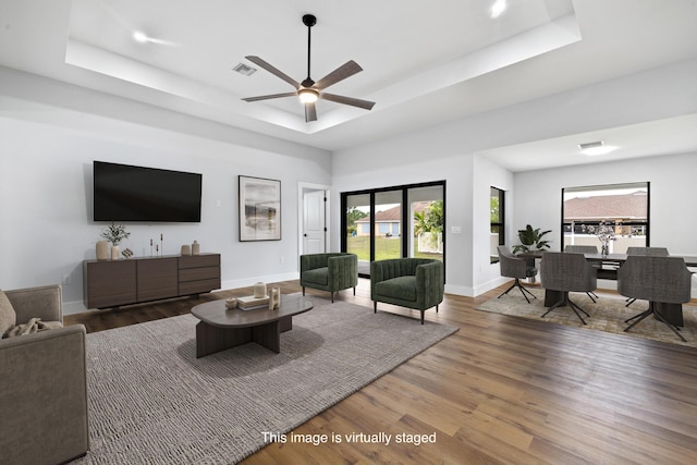 living area with a tray ceiling, visible vents, ceiling fan, wood finished floors, and baseboards