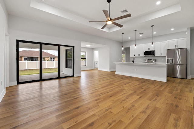 unfurnished living room with a sink, visible vents, baseboards, light wood-style floors, and a raised ceiling