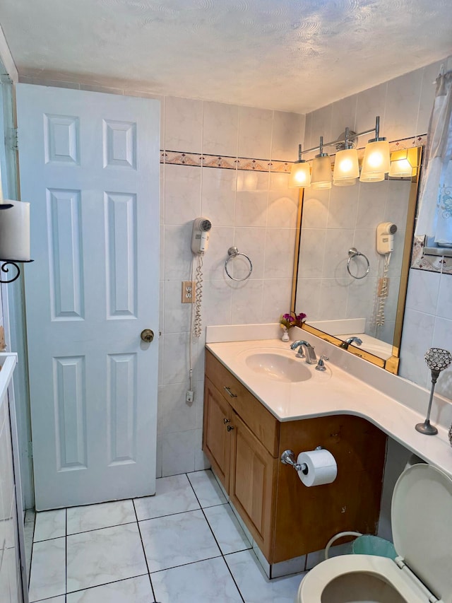 bathroom featuring a textured ceiling, vanity, tile patterned flooring, tile walls, and toilet