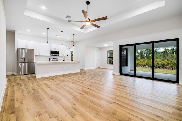 unfurnished living room featuring a raised ceiling, visible vents, light wood-style flooring, a ceiling fan, and baseboards