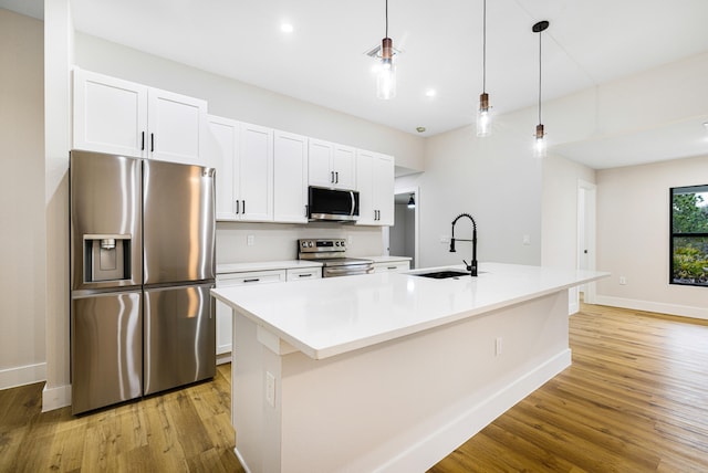 kitchen with pendant lighting, a center island with sink, light countertops, appliances with stainless steel finishes, and white cabinets