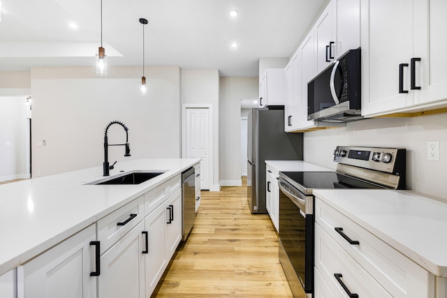 kitchen featuring a sink, white cabinetry, light countertops, appliances with stainless steel finishes, and hanging light fixtures