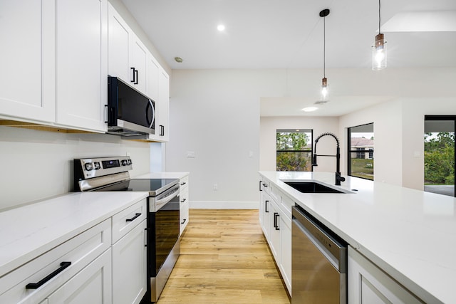 kitchen featuring light stone counters, a sink, white cabinetry, appliances with stainless steel finishes, and decorative light fixtures