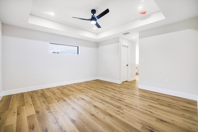 spare room with ceiling fan, a tray ceiling, and light hardwood / wood-style floors