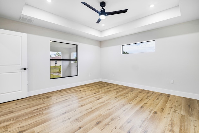 spare room with light wood-type flooring, baseboards, visible vents, and a tray ceiling