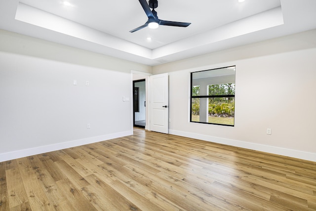 unfurnished room with a tray ceiling, recessed lighting, light wood-style flooring, ceiling fan, and baseboards