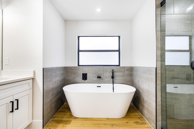 bathroom featuring vanity, plus walk in shower, wood-type flooring, and tile walls