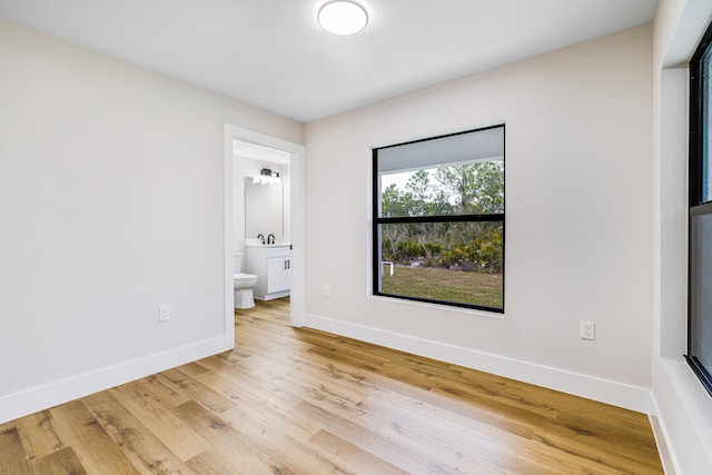 unfurnished bedroom featuring light wood-type flooring, a sink, baseboards, and ensuite bathroom