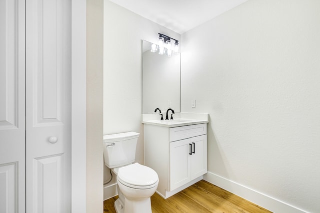 bathroom with a closet, toilet, vanity, wood finished floors, and baseboards