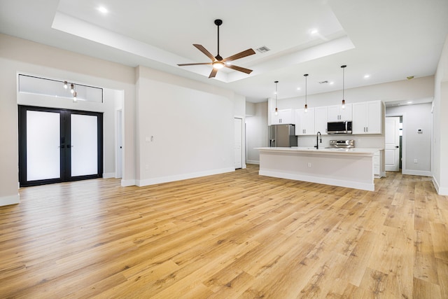 unfurnished living room featuring french doors, a raised ceiling, sink, and light hardwood / wood-style flooring