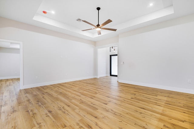 spare room featuring a ceiling fan, a raised ceiling, baseboards, and light wood finished floors