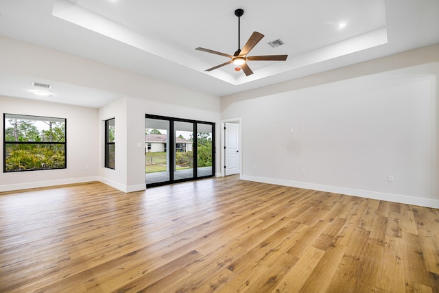 empty room with light wood finished floors, baseboards, visible vents, and a raised ceiling