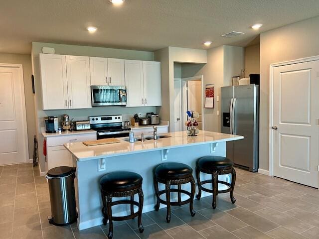 kitchen featuring a textured ceiling, a center island with sink, a kitchen bar, stainless steel appliances, and white cabinetry