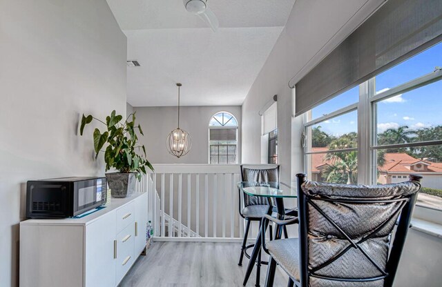 kitchen featuring white cabinets, light hardwood / wood-style flooring, ceiling fan with notable chandelier, light stone countertops, and black fridge