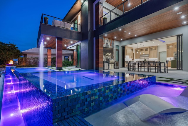 pool at night with a patio area and pool water feature