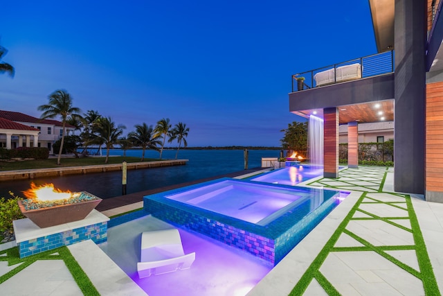 view of pool featuring a water view, a patio, a fire pit, and an in ground hot tub