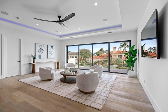 living room with a raised ceiling, light hardwood / wood-style flooring, and ceiling fan