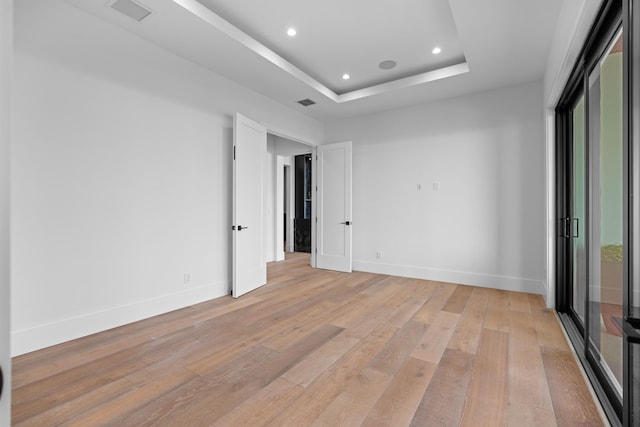 spare room with light hardwood / wood-style flooring and a raised ceiling