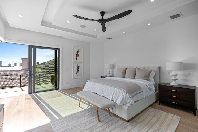 bedroom with light hardwood / wood-style flooring, ceiling fan, a tray ceiling, and access to outside