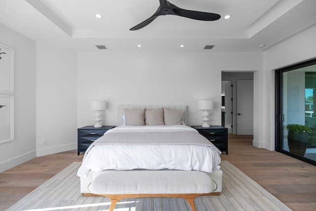 bedroom with a tray ceiling, ceiling fan, hardwood / wood-style flooring, and access to exterior