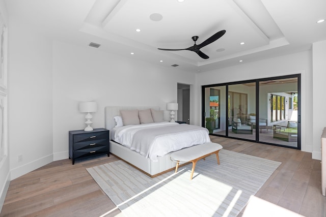 bedroom with light wood-type flooring, a tray ceiling, access to outside, and ceiling fan