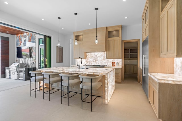 kitchen featuring light brown cabinetry, light stone countertops, sink, an island with sink, and tasteful backsplash